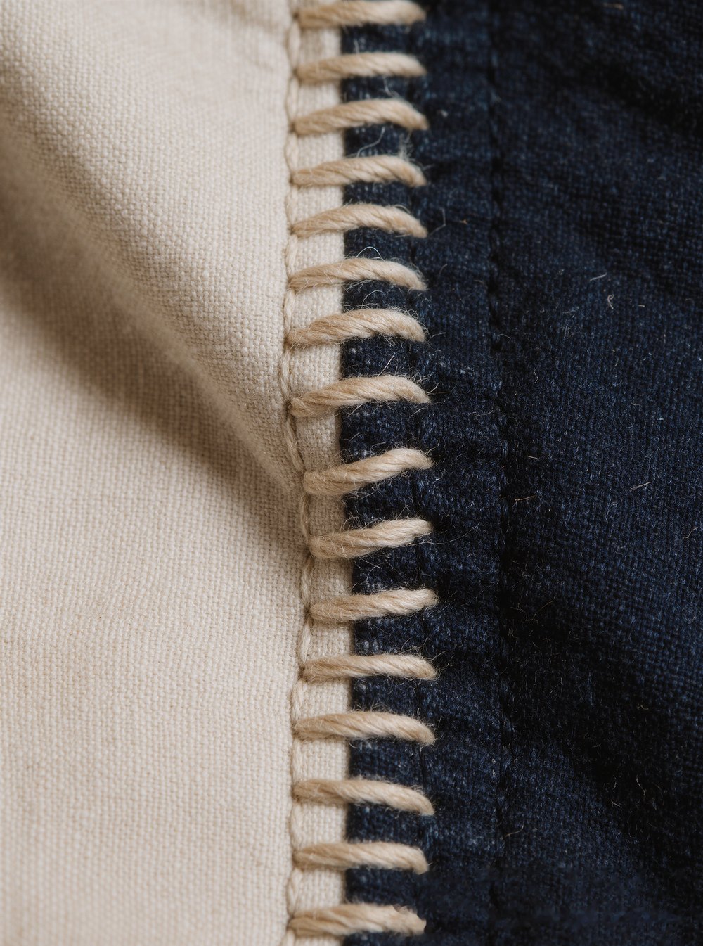 Close detail of a hand-stitched seam joining cream cotton to dark navy twill